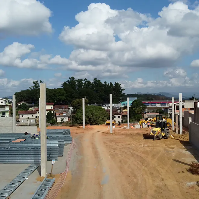 Pilares pré-moldados erguidos no terreno, com as peças da cobertura no canteiro